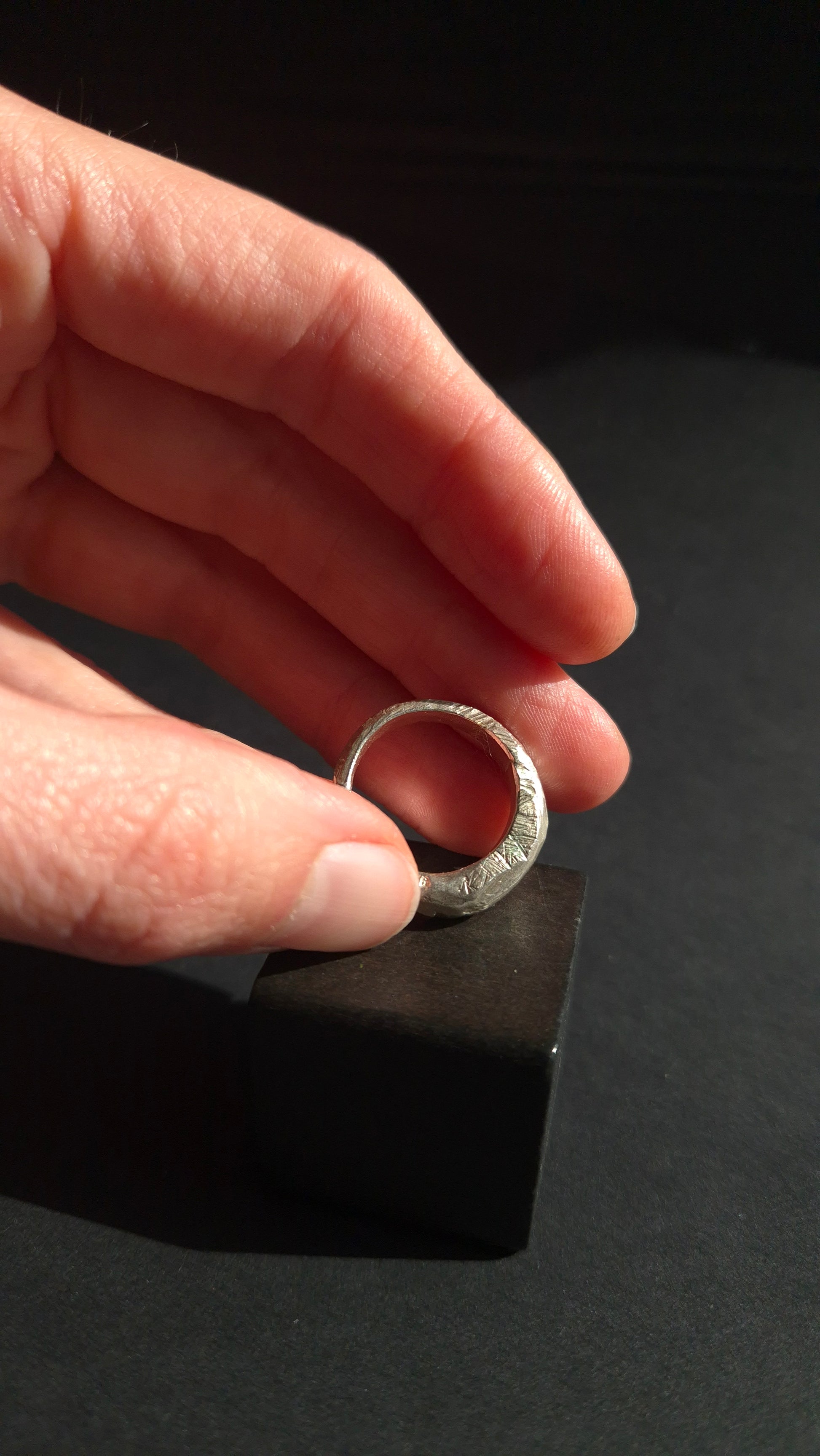 Hand holding a silver ring with a black background